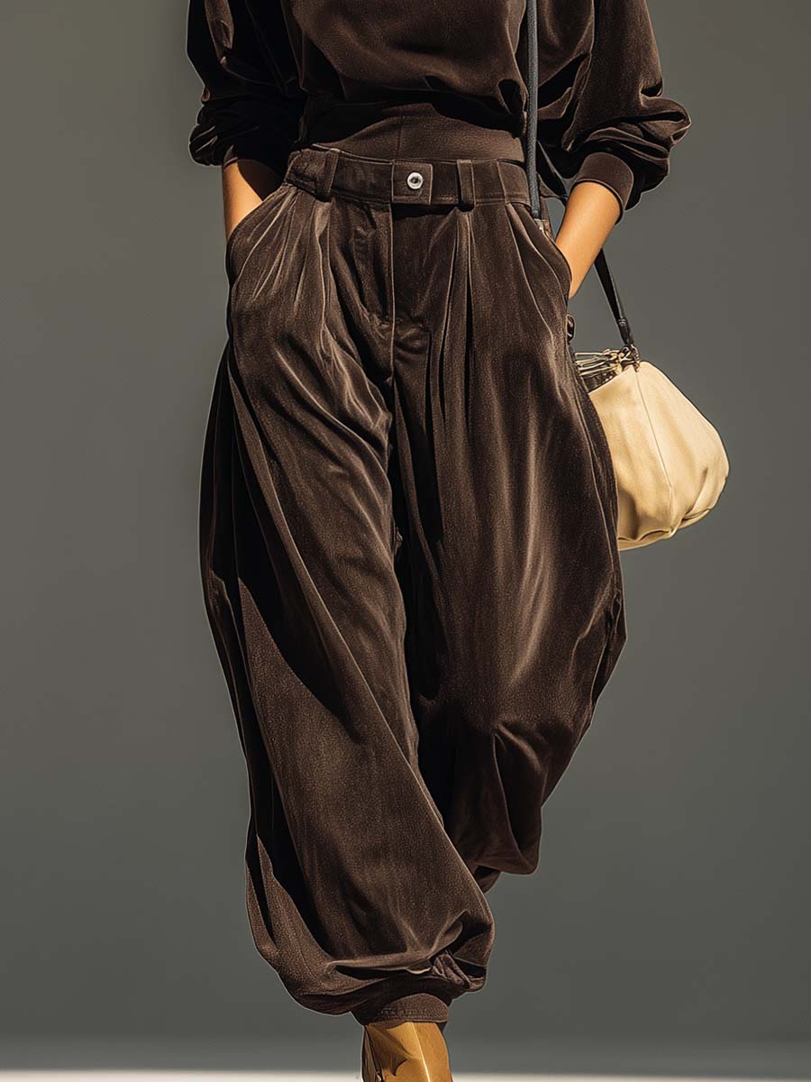 Woman wearing brown velvet cowl neck top and wide leg pants with cream-colored purse.