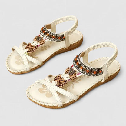 White Athena - Faux-leather flat slingback sandals featuring a beaded medallion centerpiece, embroidered instep strap, and contrast stitching along the sole edge.