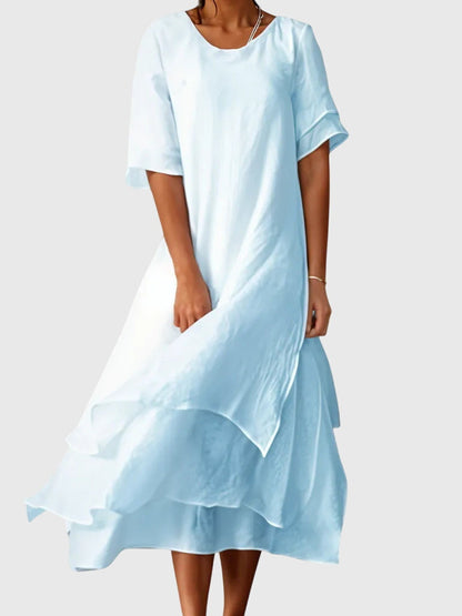 Blue - A woman wearing a light pink, double-layered chiffon midi dress with short sleeves, a scoop neck, and a flowy asymmetric hemline.