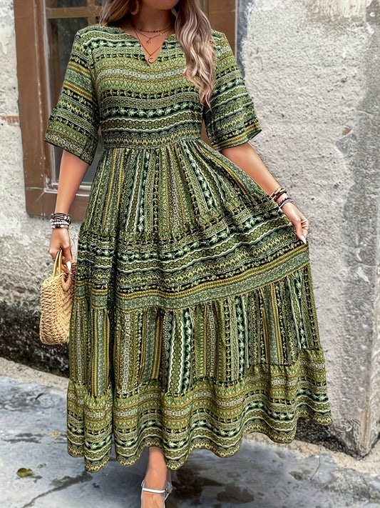 A woman wearing an olive green bohemian geometric print maxi sundress with a V-neckline, elbow-length sleeves, and a tiered skirt, holding a small woven straw handbag.