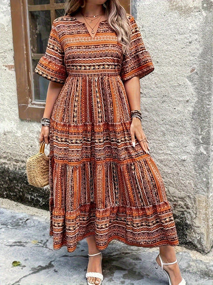 Brown - A woman wearing an olive green bohemian geometric print maxi sundress with a V-neckline, elbow-length sleeves, and a tiered skirt, holding a small woven straw handbag.