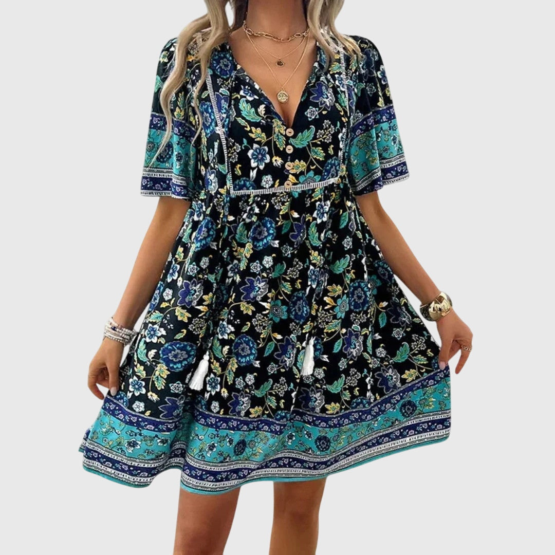 Navy Blue - A woman wearing a peach-colored bohemian mini sundress featuring a pink and burgundy paisley floral print, short sleeves, a V-neckline with tassel ties, and a border print hem.