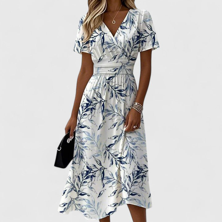 White - A woman wearing a white midi dress featuring a blue botanical leaf print, a surplice V-neckline, flutter sleeves, and a defined banded waist.