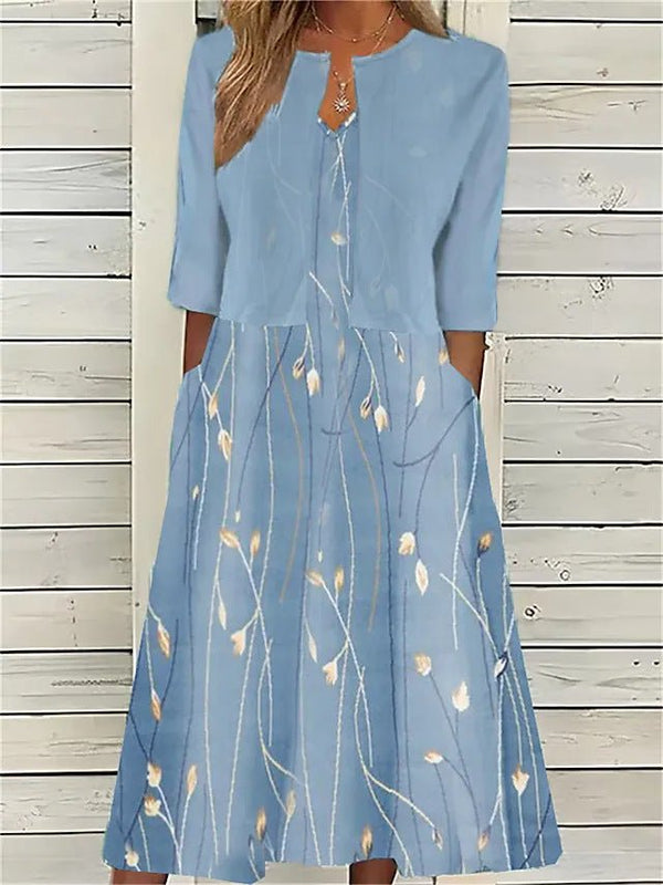 A woman wearing a dusty blue mock-layered midi dress featuring a solid 3/4-sleeve bodice, a split neckline, and a flowy skirt with a white botanical branch print.