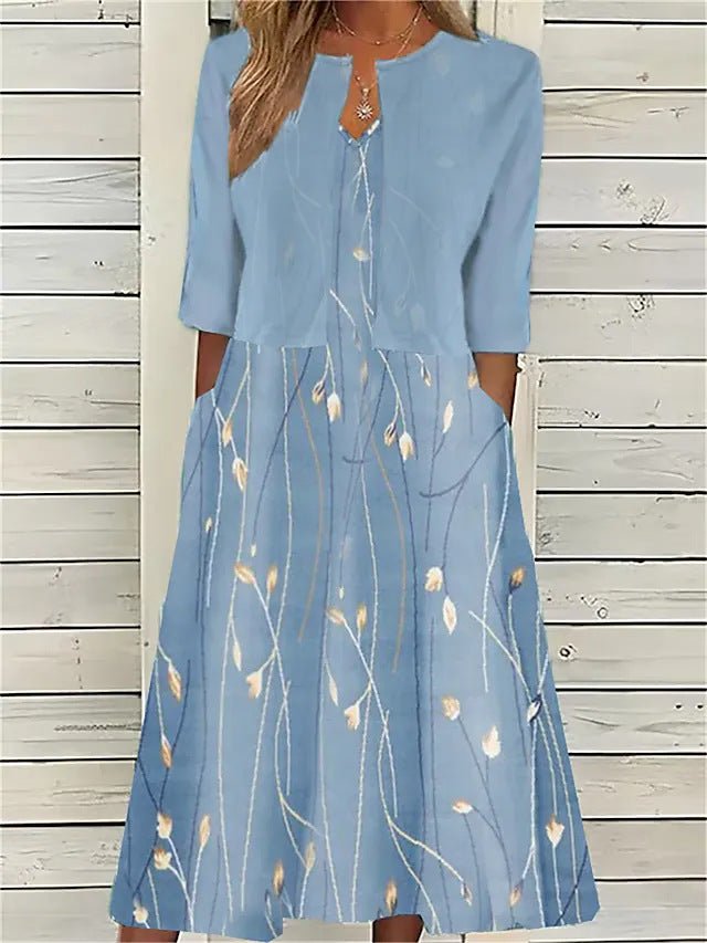 A woman wearing a dusty blue mock-layered midi dress featuring a solid 3/4-sleeve bodice, a split neckline, and a flowy skirt with a white botanical branch print.