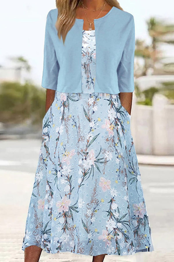 Light Blue - A woman wearing a dusty blue mock-layered midi dress featuring a solid 3/4-sleeve bodice, a split neckline, and a flowy skirt with a white botanical branch print.