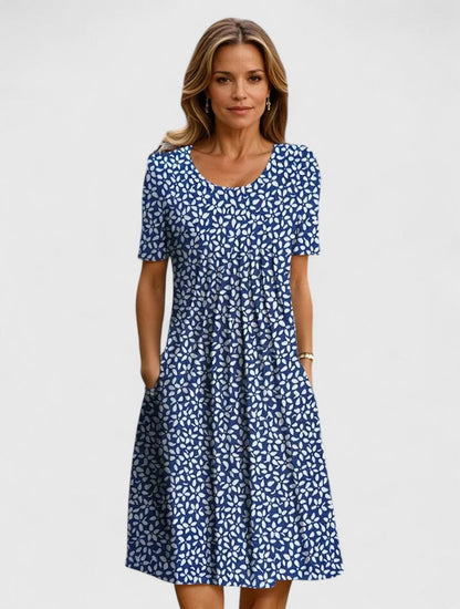 Blue Flowers - A woman wearing a white short-sleeve A-line sundress featuring a vibrant yellow and blue wildflower botanical print, complete with a scoop neckline and side pockets.
