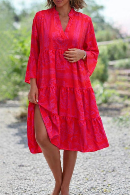 Red - A woman wearing a vibrant red and pink tropical botanical print midi sundress with three-quarter bell sleeves, a split V-neckline, and a tiered flowy skirt.