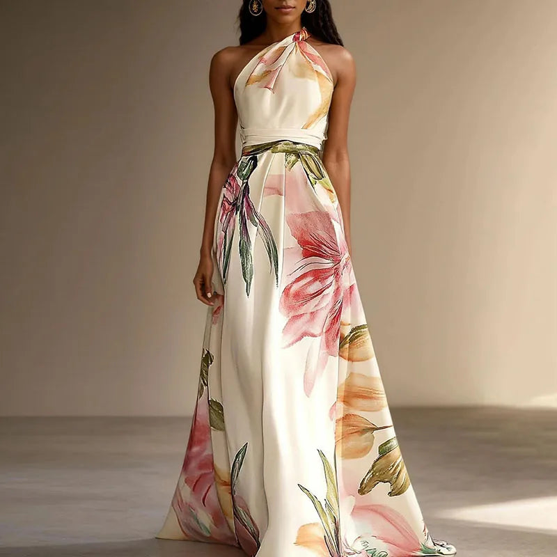 Cream - A woman wearing a floor-length satin halter maxi dress featuring a large-scale watercolor botanical print in pink, orange, and green on an ivory background, showcasing a pleated waist and a flowing A-line silhouette.