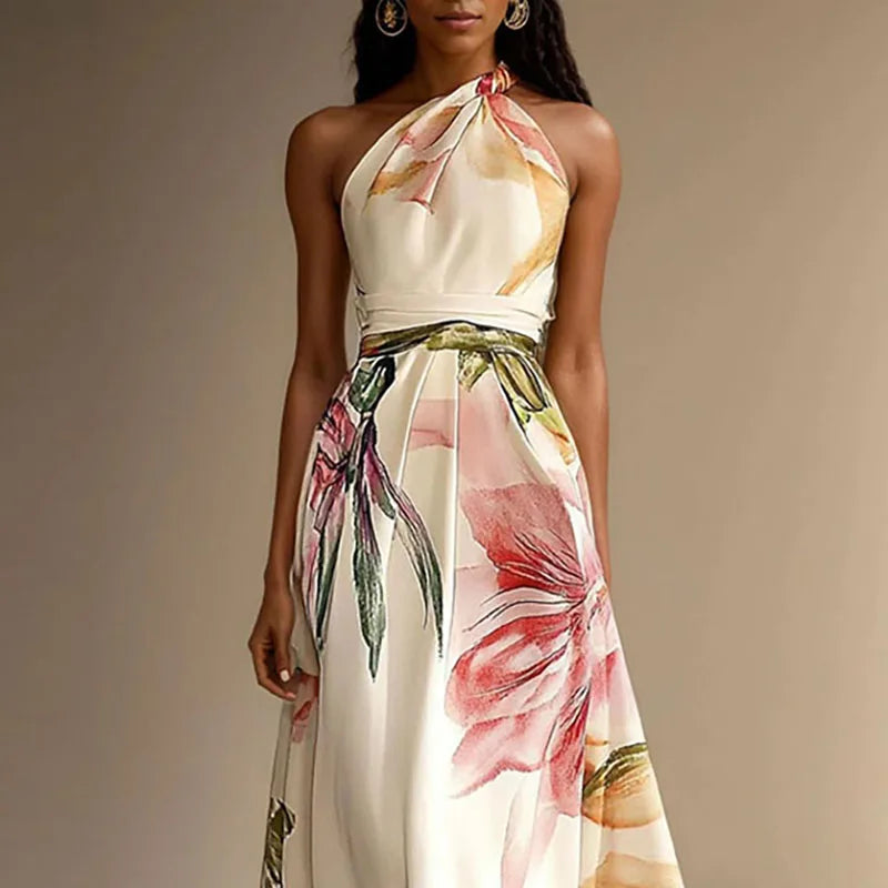Cream - A woman wearing a floor-length satin halter maxi dress featuring a large-scale watercolor botanical print in pink, orange, and green on an ivory background, showcasing a pleated waist and a flowing A-line silhouette.
