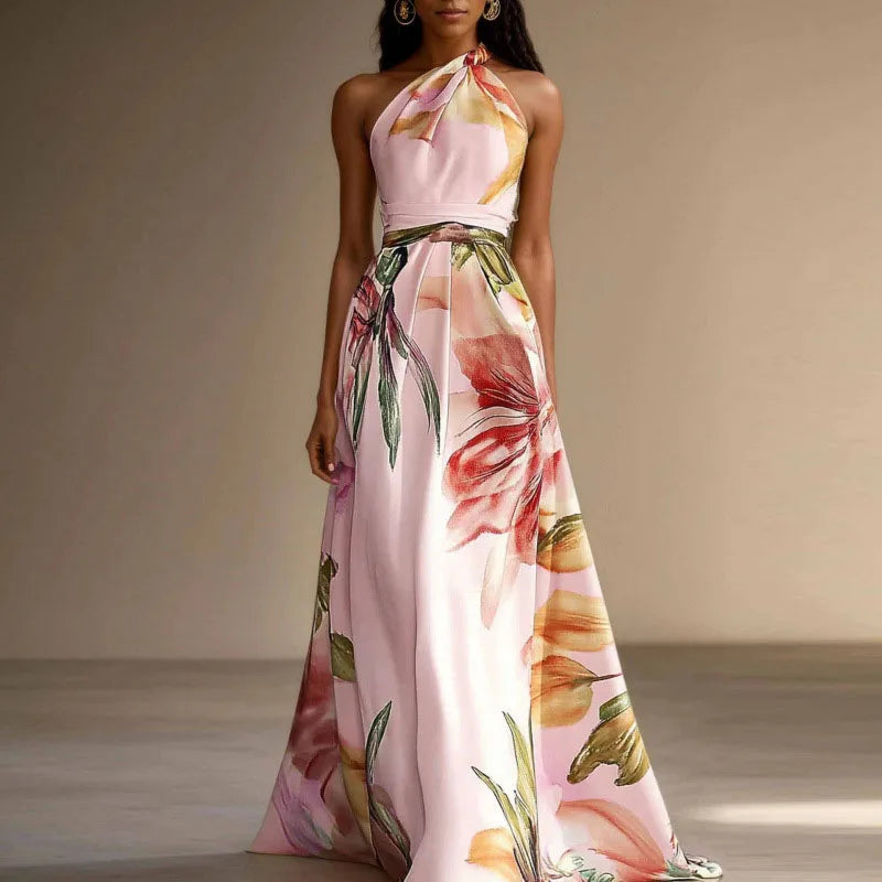 Pink - A woman wearing a floor-length satin halter maxi dress featuring a large-scale watercolor botanical print in pink, orange, and green on an ivory background, showcasing a pleated waist and a flowing A-line silhouette.