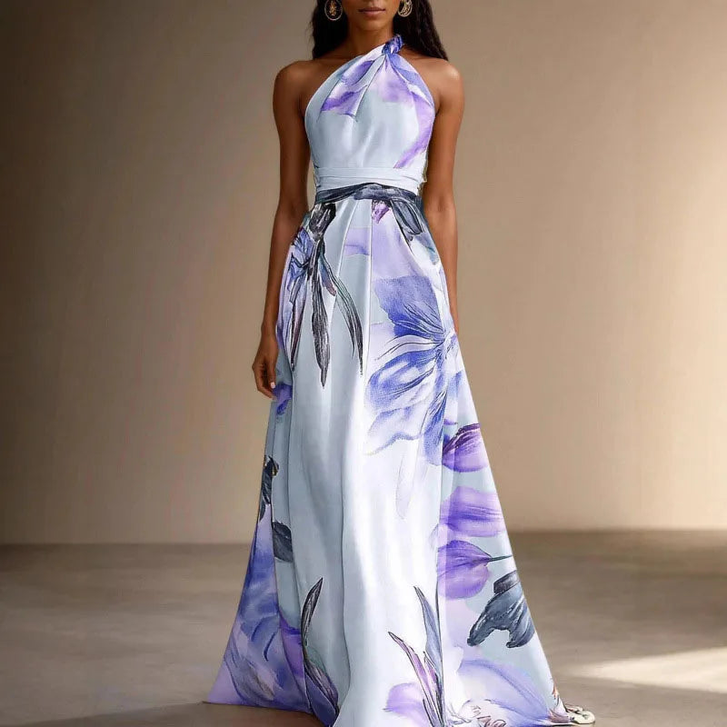 Blue - A woman wearing a floor-length satin halter maxi dress featuring a large-scale watercolor botanical print in pink, orange, and green on an ivory background, showcasing a pleated waist and a flowing A-line silhouette.