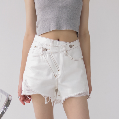 Woman wearing light wash denim shorts with asymmetrical waist and distressed hem.