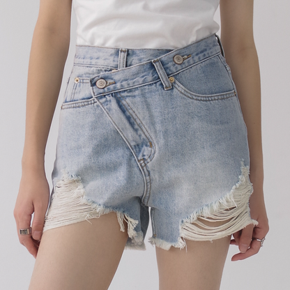 Woman wearing light wash denim shorts with asymmetrical waist and distressed hem.