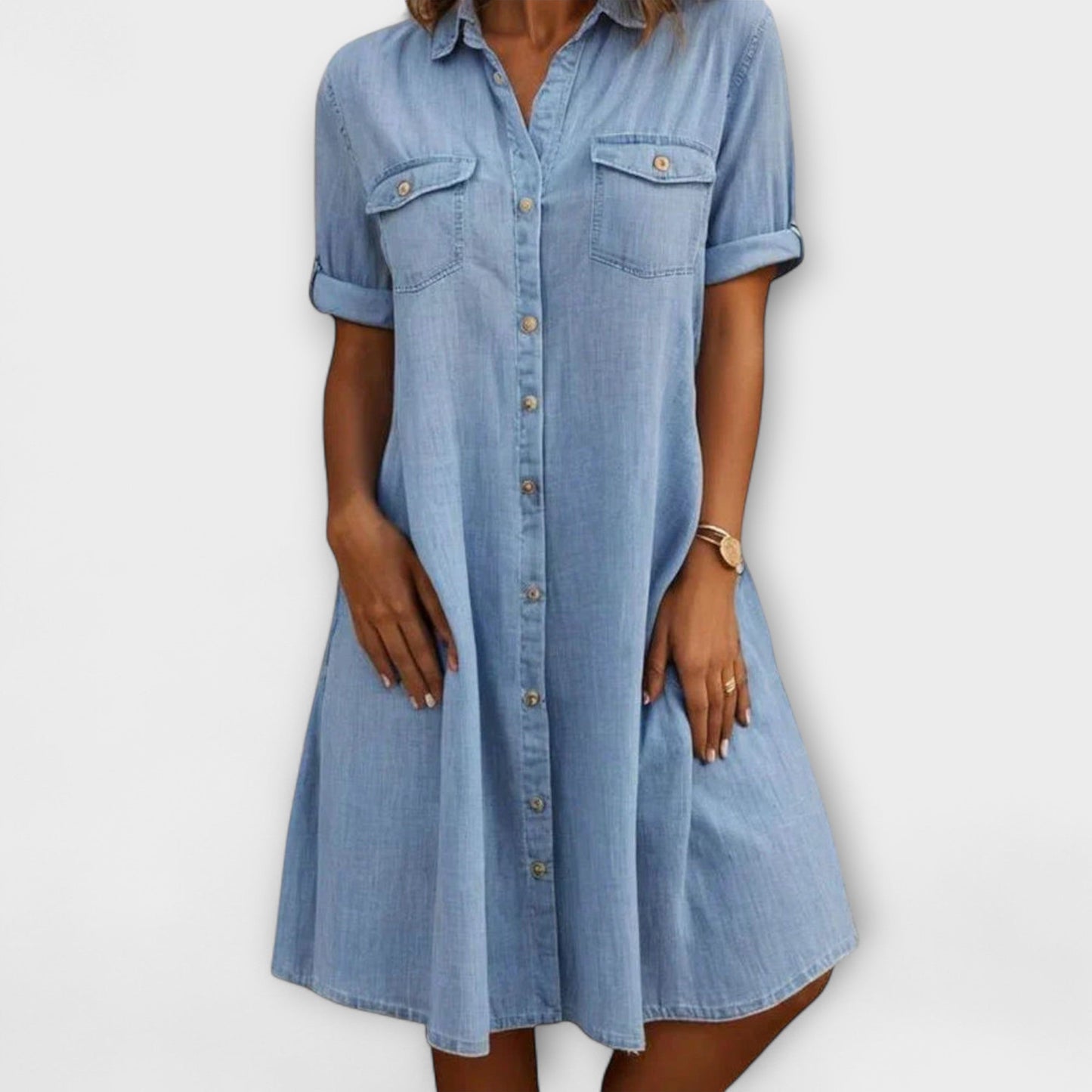 Blue - A woman wearing a light blue chambray short-sleeve button-down sundress with chest pockets and a relaxed fit.