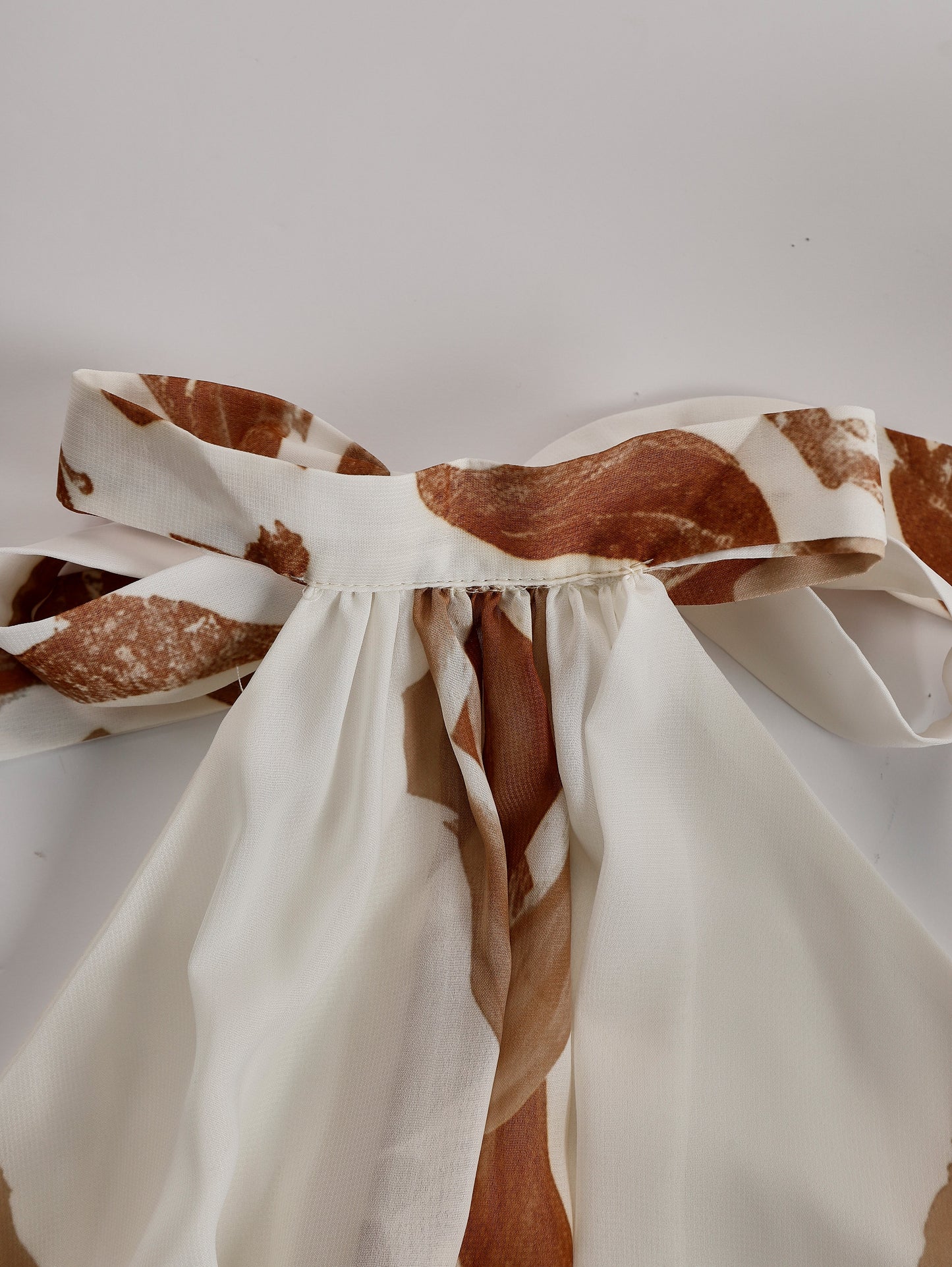 Cream - Sleeveless halter neck maxi dress featuring an abstract print, gathered waist, and double front slits with button accents.