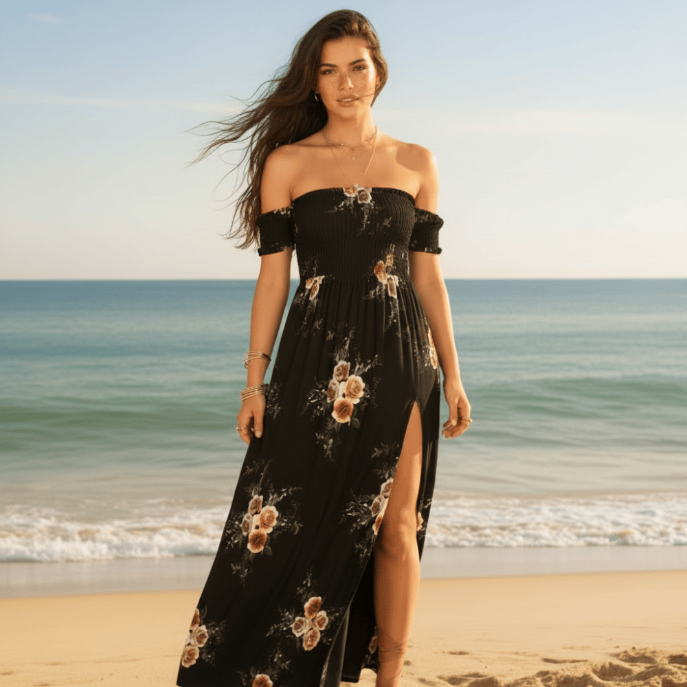 Black - A woman standing on a sandy beach wearing a white off-the-shoulder chiffon maxi dress with a botanical floral print, featuring a smocked bodice and a high thigh slit.