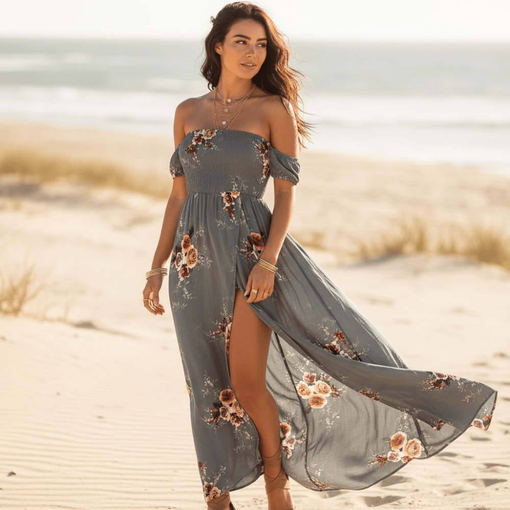 Gray - A woman standing on a sandy beach wearing a white off-the-shoulder chiffon maxi dress with a botanical floral print, featuring a smocked bodice and a high thigh slit.
