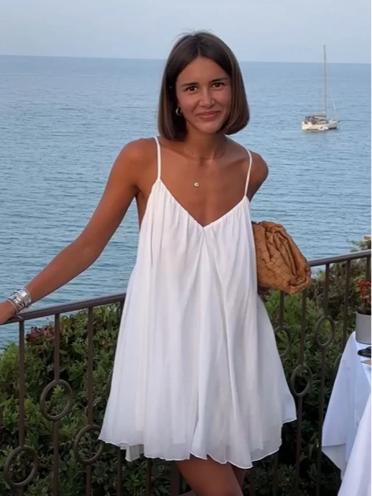 3XL - Woman wearing a short, flowy chiffon babydoll mini sundress with spaghetti straps and a gathered neckline, standing outdoors near an ocean