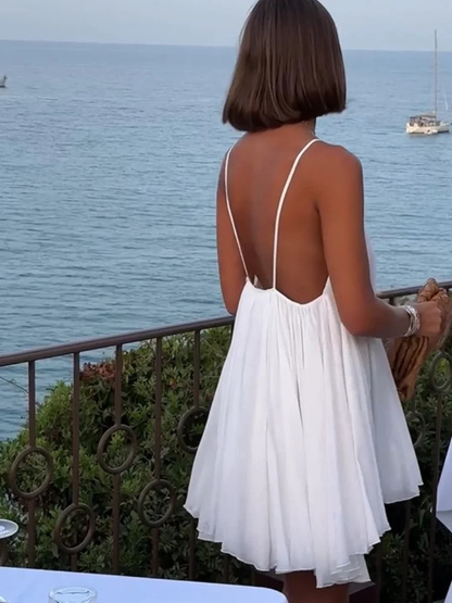 3XL - Woman wearing a short, flowy chiffon babydoll mini sundress with spaghetti straps and a gathered neckline, standing outdoors near an ocean