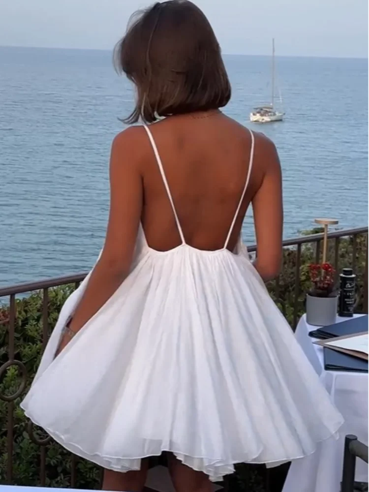 3XL - Woman wearing a short, flowy chiffon babydoll mini sundress with spaghetti straps and a gathered neckline, standing outdoors near an ocean
