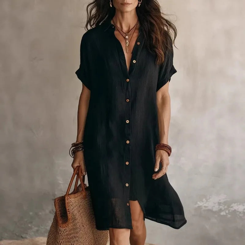 Black - A woman wearing a black, short-sleeved linen midi shirt dress with a button-down front, styled with a woven straw tote bag.