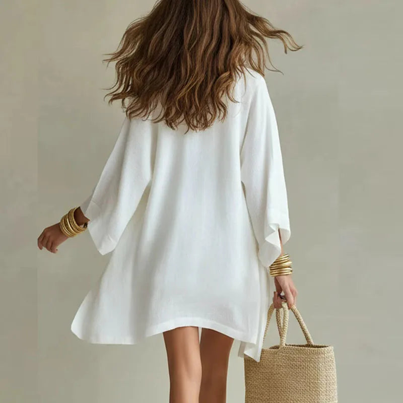 White - A woman wearing a white three-piece linen set featuring a V-neck tank top, high-waisted drawstring shorts, and a matching long open-front duster cardigan, accessorized with gold layered necklaces and a woven straw bag.