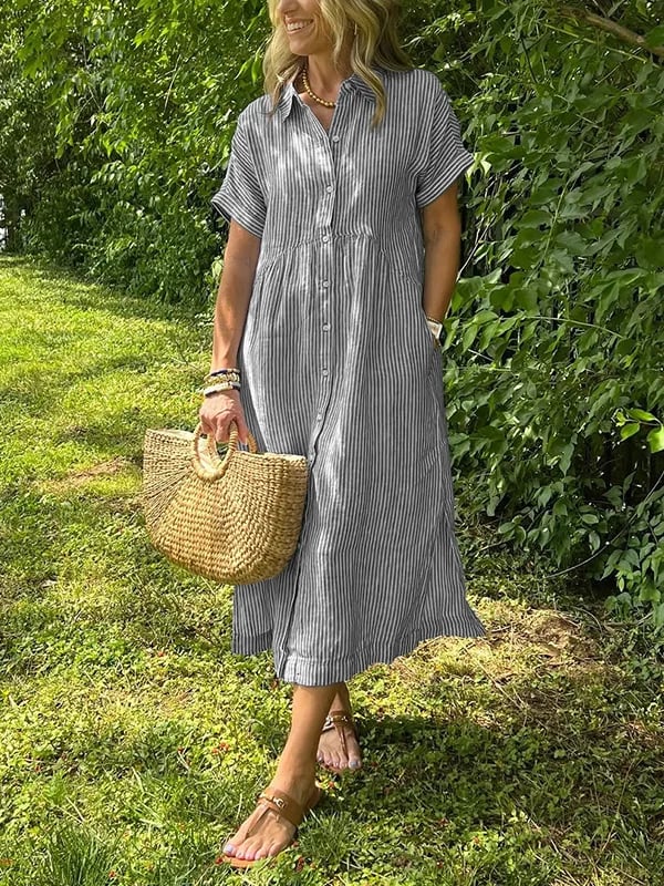 Grey - A woman wearing a blue and white vertically striped linen-blend midi shirt dress with short sleeves, a pointed collar, and a button-down front, holding a woven straw bag in a grassy outdoor setting.