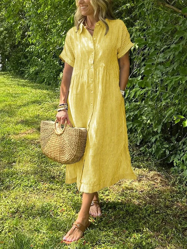 Yellow - A woman wearing a blue and white vertically striped linen-blend midi shirt dress with short sleeves, a pointed collar, and a button-down front, holding a woven straw bag in a grassy outdoor setting.