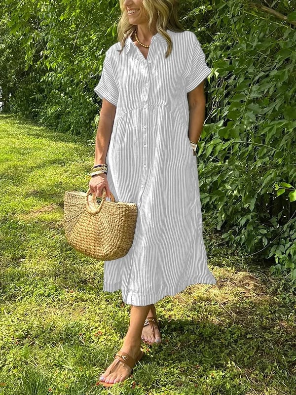 White - A woman wearing a blue and white vertically striped linen-blend midi shirt dress with short sleeves, a pointed collar, and a button-down front, holding a woven straw bag in a grassy outdoor setting.