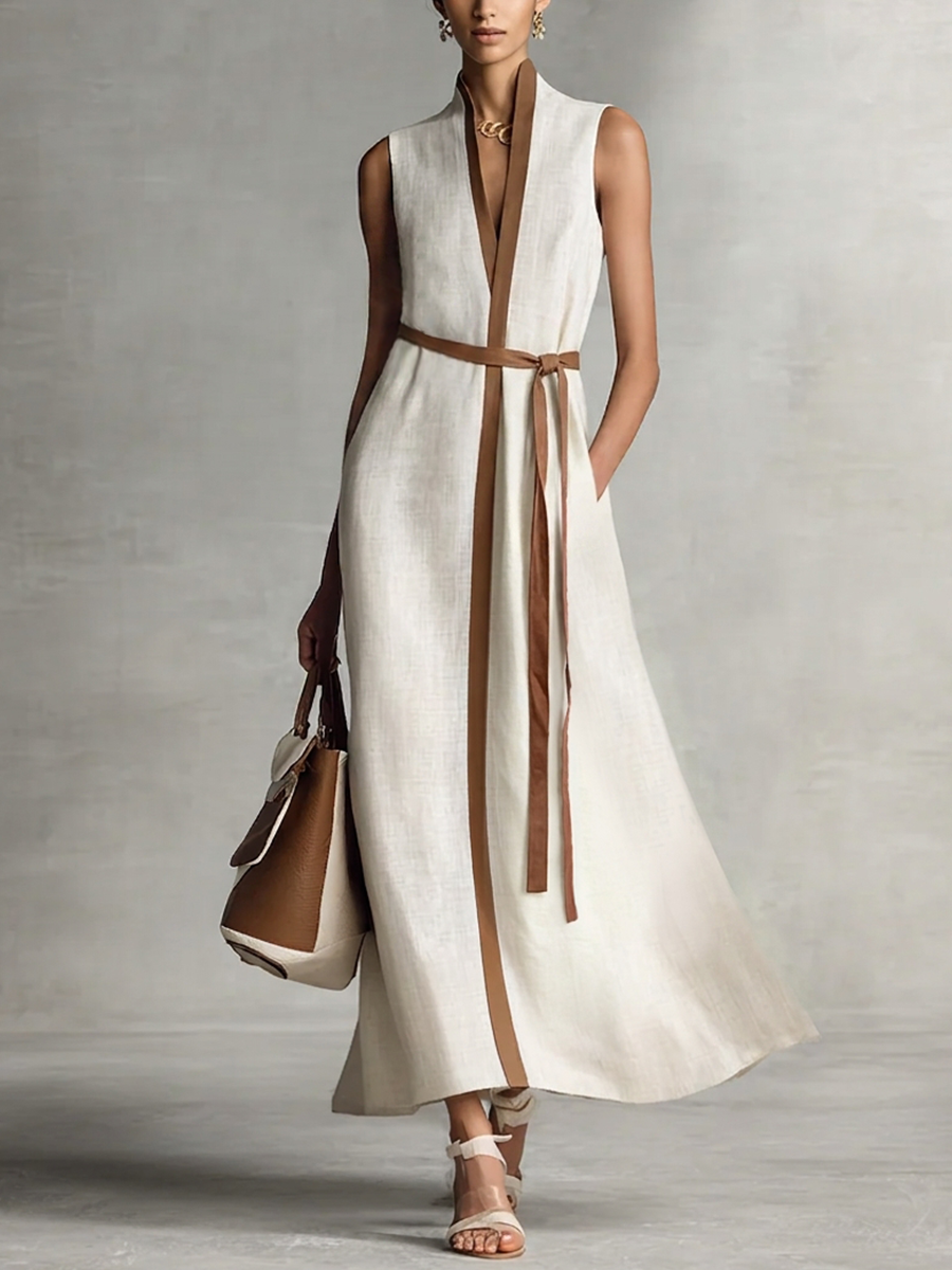 White and brown - A model wearing a sleeveless woven maxi dress featuring a deep V-neck, contrasting front trim, and a waist tie, styled with a structured handbag.