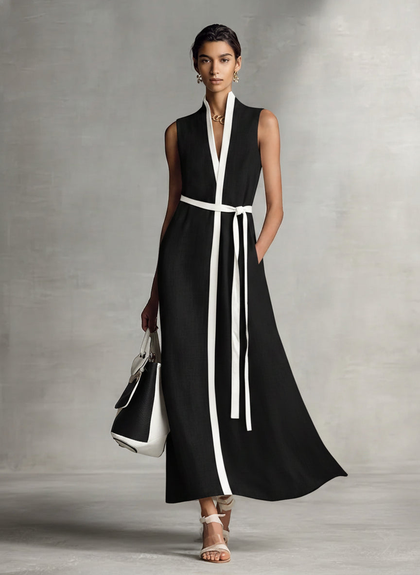 Black and white - A model wearing a sleeveless woven maxi dress featuring a deep V-neck, contrasting front trim, and a waist tie, styled with a structured handbag.