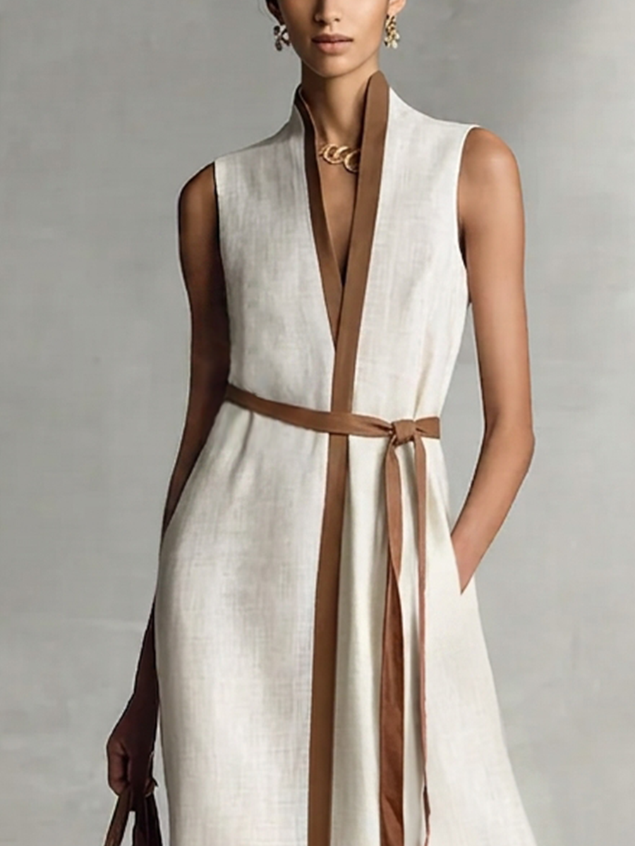 Black and white - A model wearing a sleeveless woven maxi dress featuring a deep V-neck, contrasting front trim, and a waist tie, styled with a structured handbag.