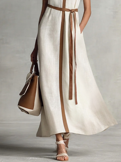 Black and white - A model wearing a sleeveless woven maxi dress featuring a deep V-neck, contrasting front trim, and a waist tie, styled with a structured handbag.