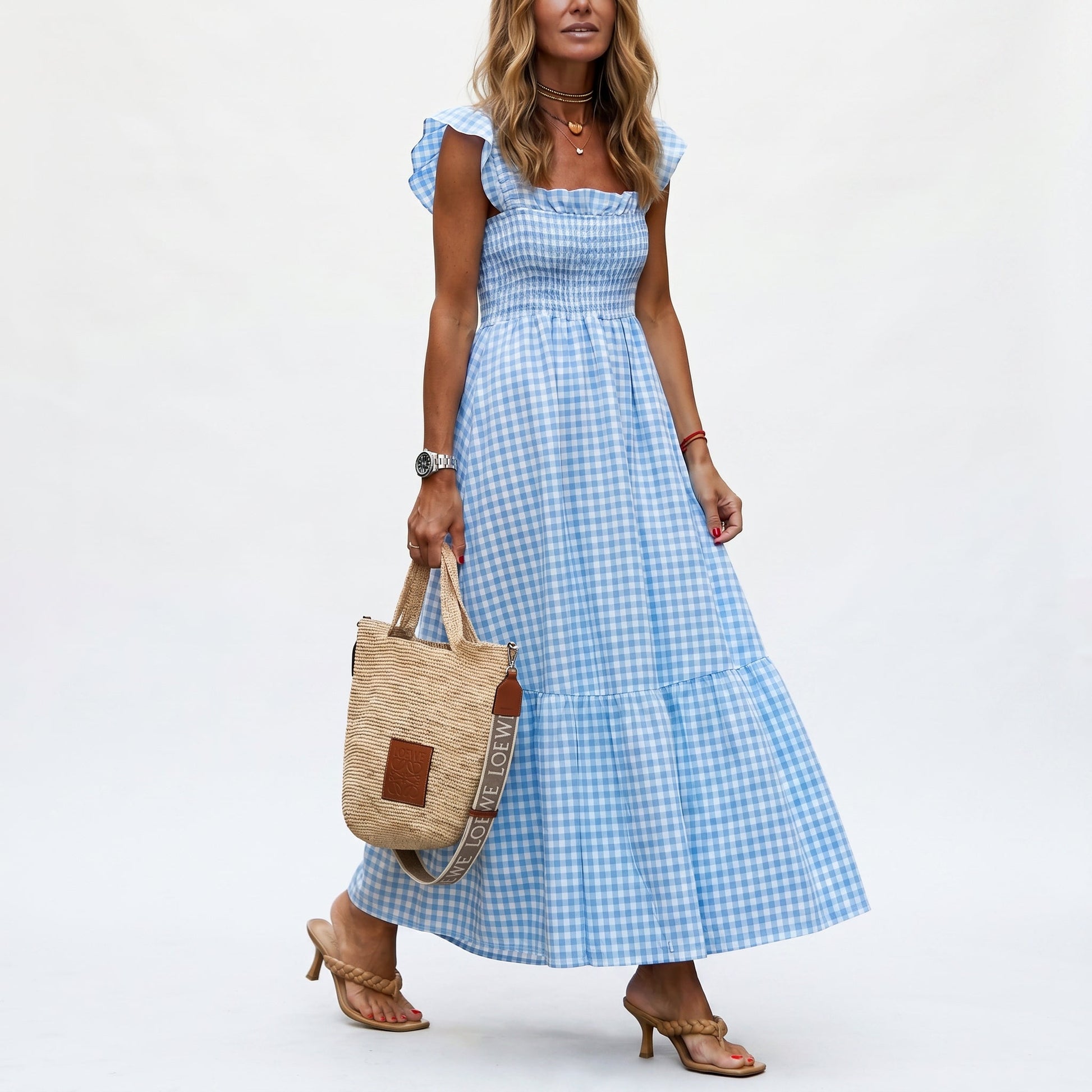 Blue - Woman wearing a gingham smocked maxi dress with flutter sleeves and a tiered skirt on a white background
