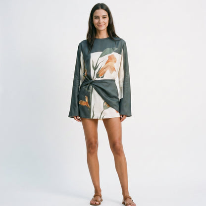 XXL - Model wearing a long-sleeve mini dress featuring a large-scale botanical print, high neckline, and an architectural twisted waist detail.