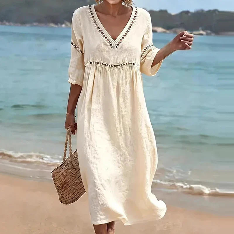 Beige - Woman walking on a beach wearing a solid colored midi dress with half sleeves, an empire waist, and crochet trim detailing