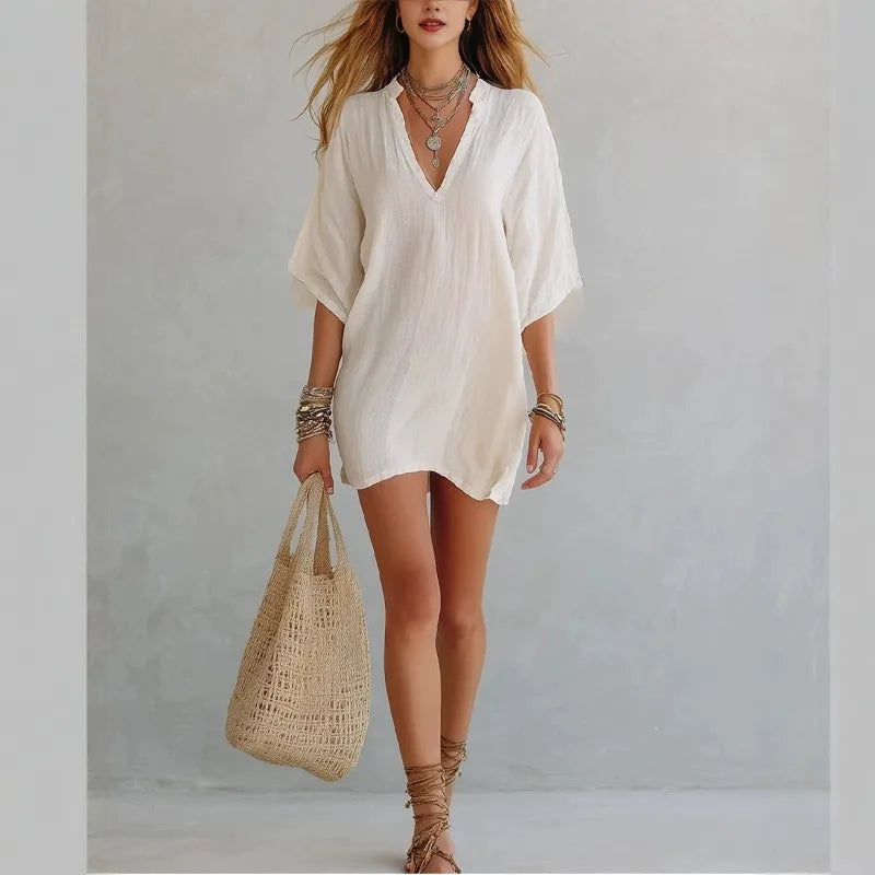 White - Woman wearing a loose-fitting mini dress with dolman sleeves and a notch neckline, carrying a woven tote bag