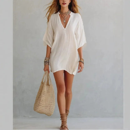 White - Woman wearing a loose-fitting mini dress with dolman sleeves and a notch neckline, carrying a woven tote bag