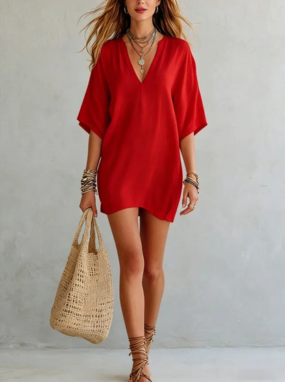 Red - Woman wearing a loose-fitting mini dress with dolman sleeves and a notch neckline, carrying a woven tote bag