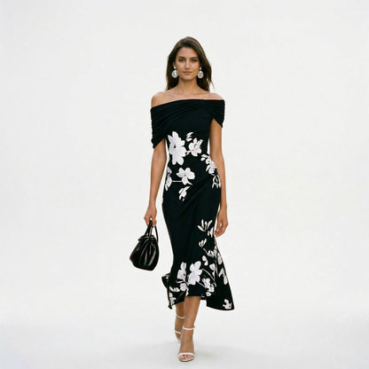 Black - Model wearing a green floral off-shoulder midi dress with a draped neckline and asymmetrical hem, holding a matching clutch.