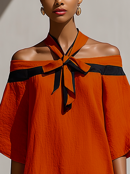 Orange - Model walking outdoors wearing a relaxed textured shift mini dress featuring a contrast halter tie neckline and draped off-the-shoulder sleeves.