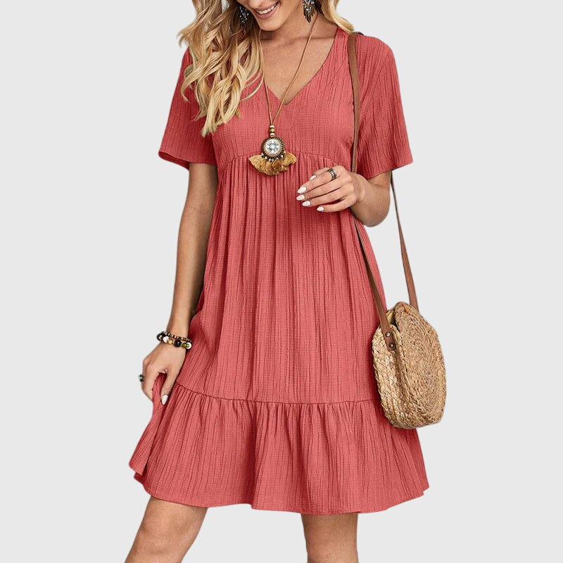 Red - A woman wearing a dusty rose crinkle gauze short-sleeve V-neck sundress with an empire waist and tiered ruffle hem, styled with a straw shoulder bag.