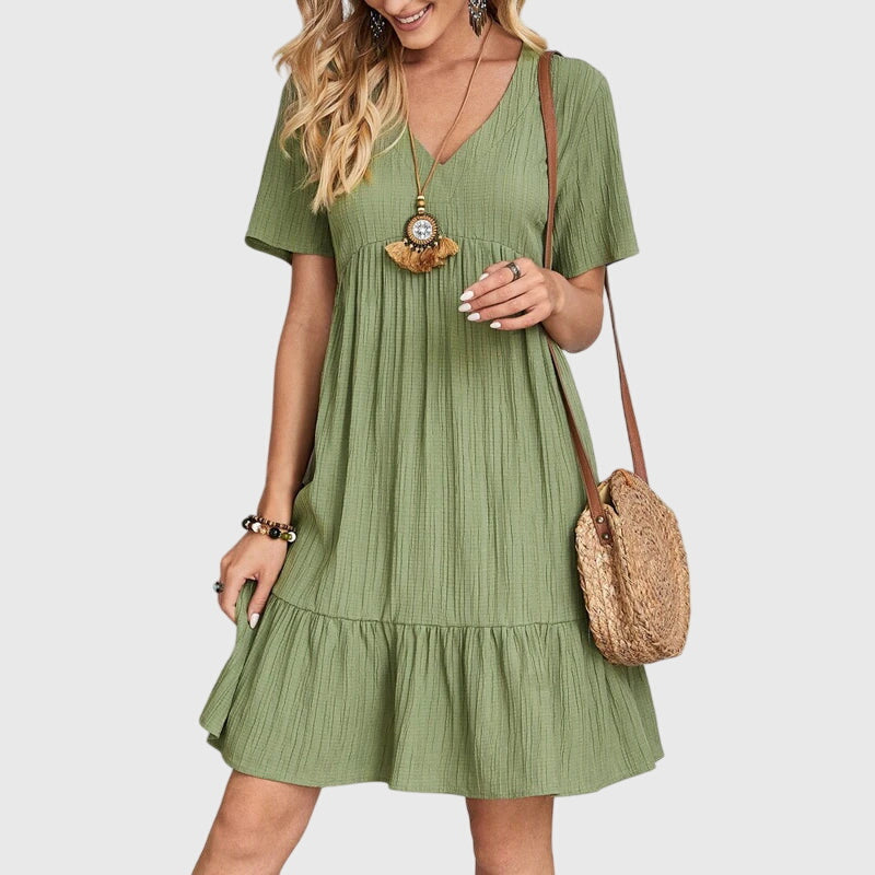 Green - A woman wearing a dusty rose crinkle gauze short-sleeve V-neck sundress with an empire waist and tiered ruffle hem, styled with a straw shoulder bag.