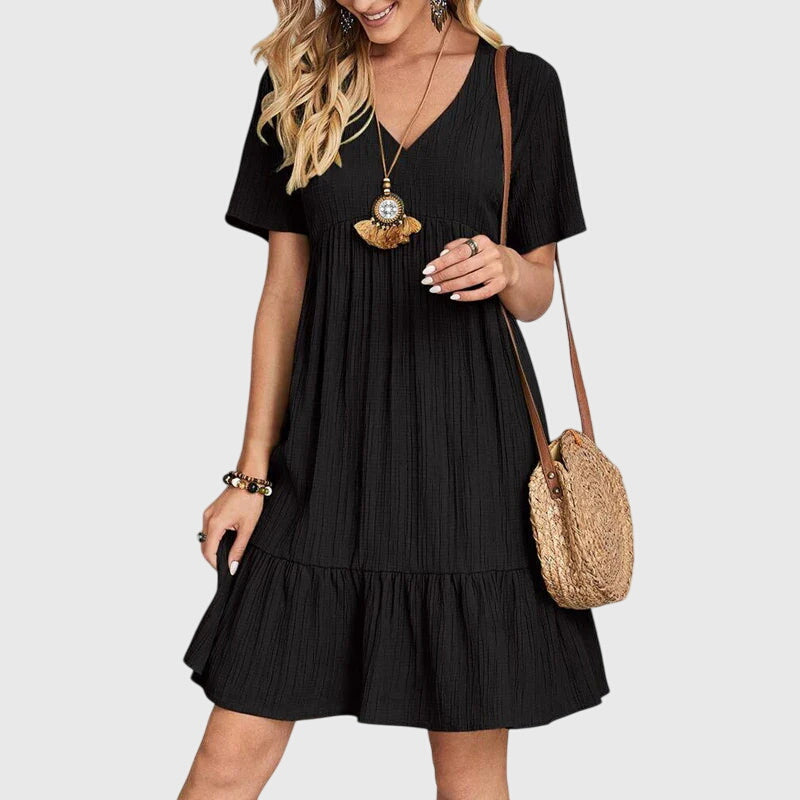 Black - A woman wearing a dusty rose crinkle gauze short-sleeve V-neck sundress with an empire waist and tiered ruffle hem, styled with a straw shoulder bag.