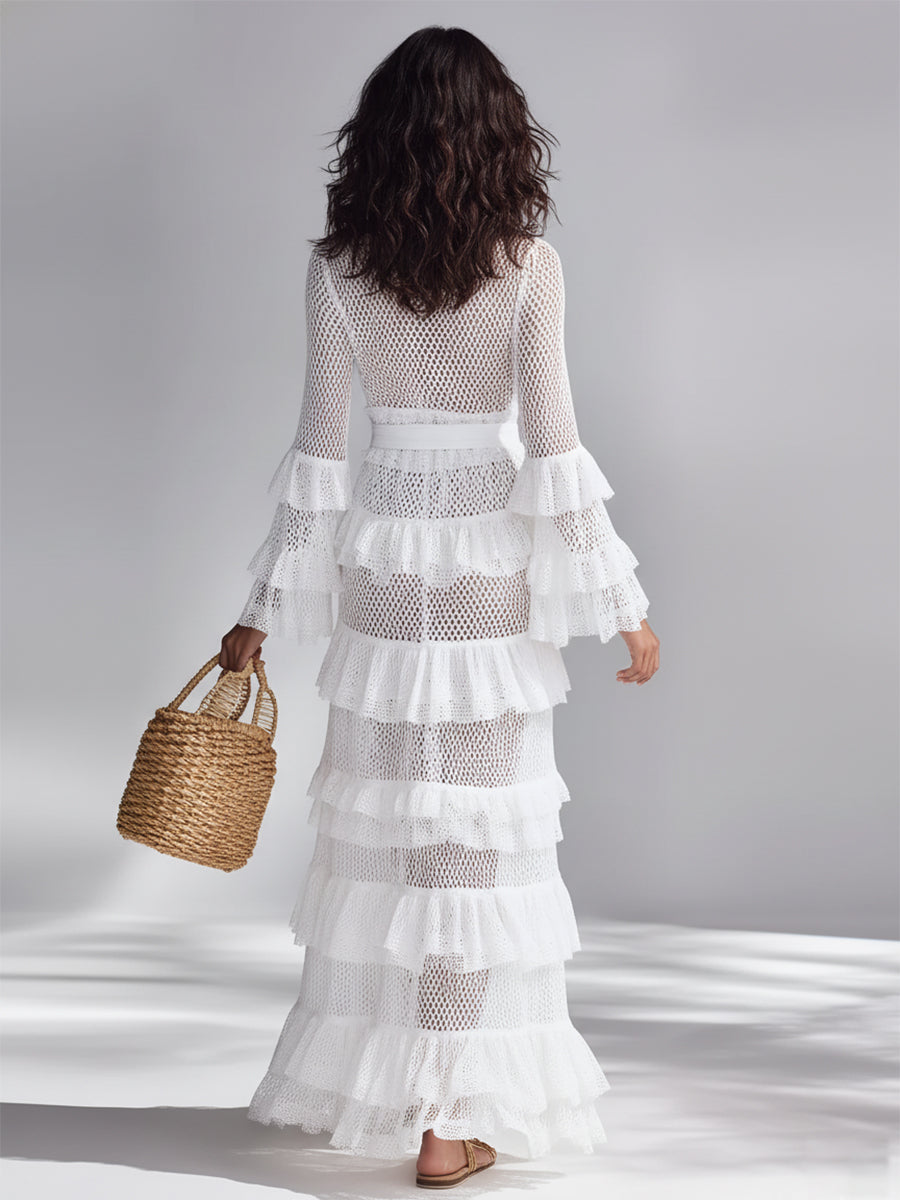 White - Woman wearing a crochet tiered maxi dress with long bell sleeves, a plunging neckline, and a waist tie, holding a woven basket bag