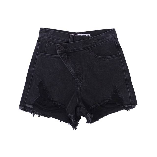 Woman wearing light wash denim shorts with asymmetrical waist and distressed hem.