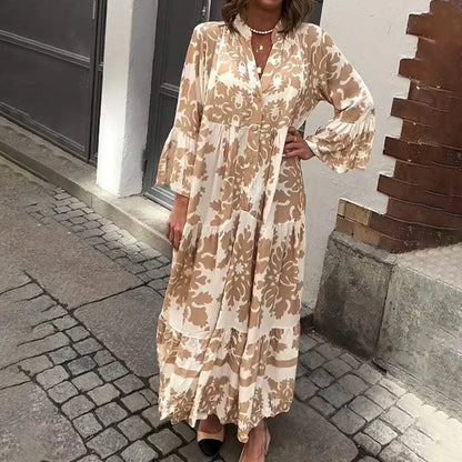 Brown - A woman wearing a cream and tan damask print maxi sundress with long bell sleeves, a V-neckline, and a tiered skirt, standing on a cobblestone street.