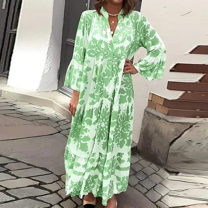 Green - A woman wearing a cream and tan damask print maxi sundress with long bell sleeves, a V-neckline, and a tiered skirt, standing on a cobblestone street.