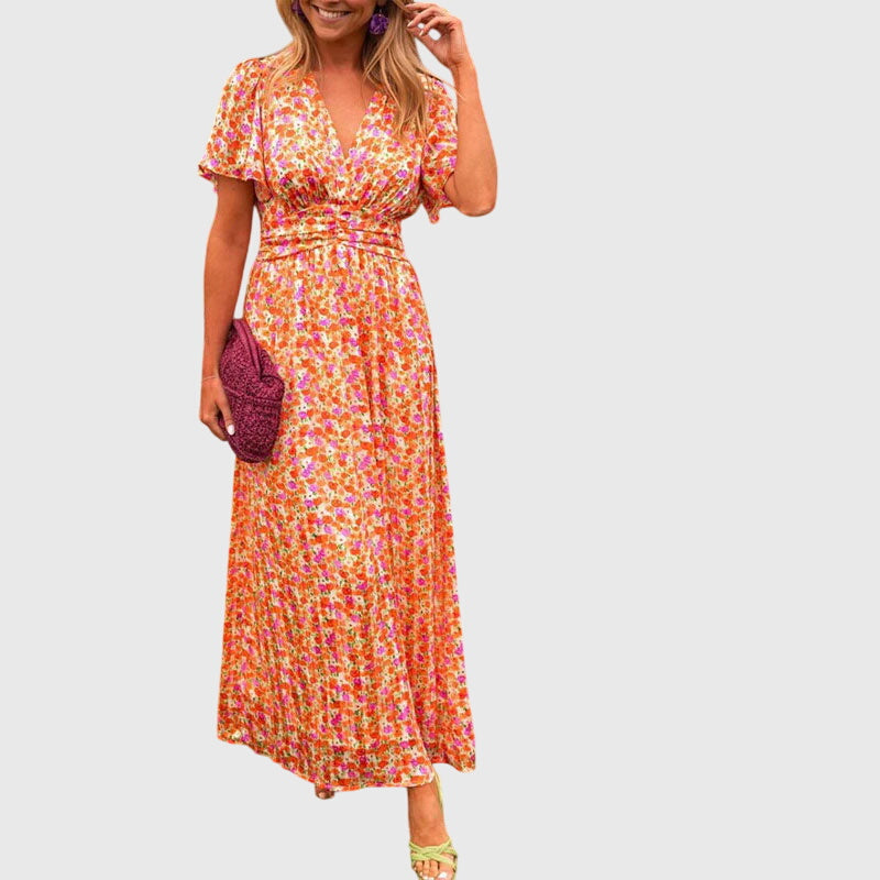 Green - A woman wearing an orange and pink ditsy floral print maxi dress with a V-neckline, flutter sleeves, and a ruched empire waist.